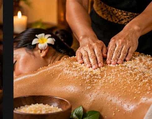 Massage therapist applying an exfoliating body scrub to a client's back during a relaxing spa treatment.
