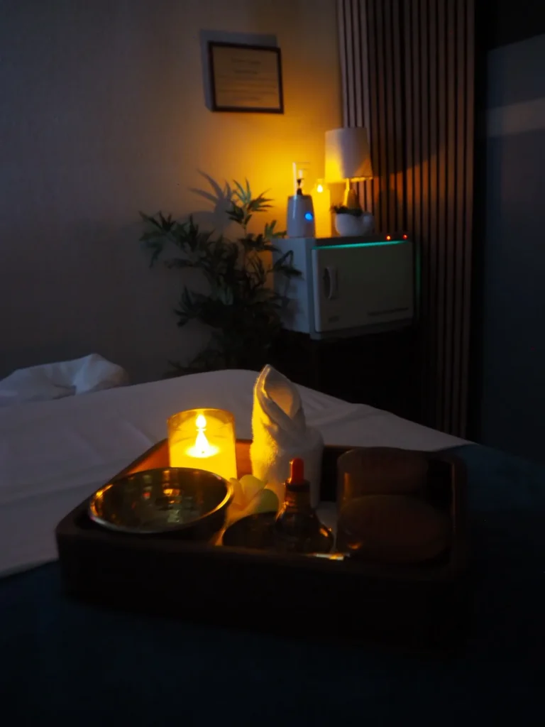 Close view of lit candles and a brass bowl on a wooden tray at the massage table